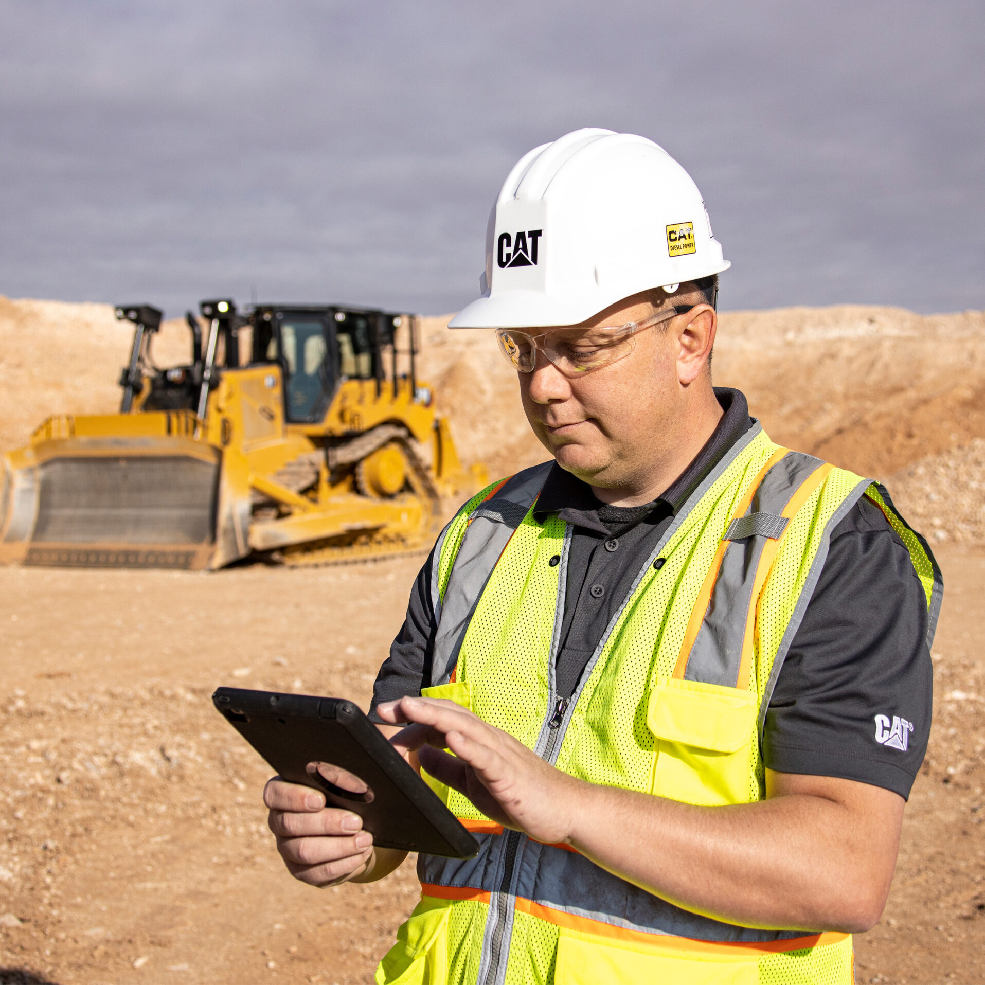 Construction worker in Cat gear using an iPad with heavy equipment in the background